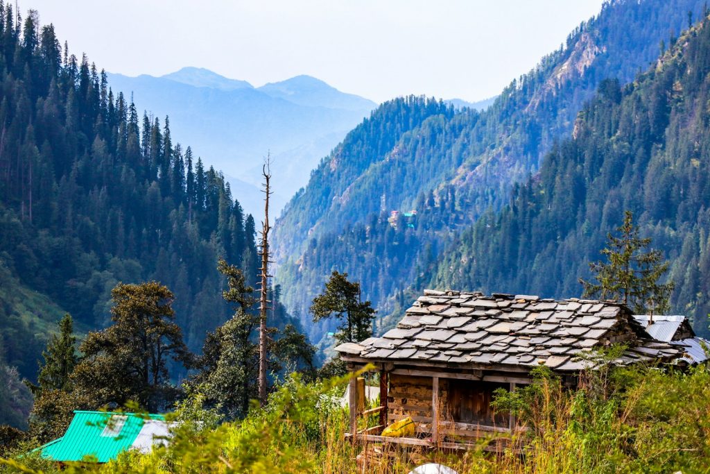 brown wooden house on green grass field near green trees and mountains during daytime