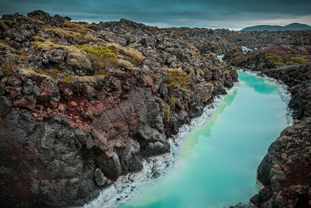 brown and green rock formation beside body of water during daytime